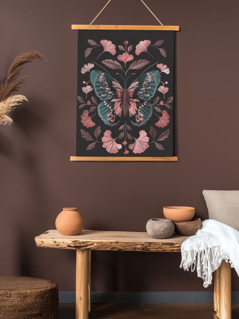 Hanging tapestry featuring a teal and pink butterfly surrounded by ginkgo-like leaves on a black background. The textile is suspended from wooden dowels with twine, creating detailed 3D embroidery-like texture.